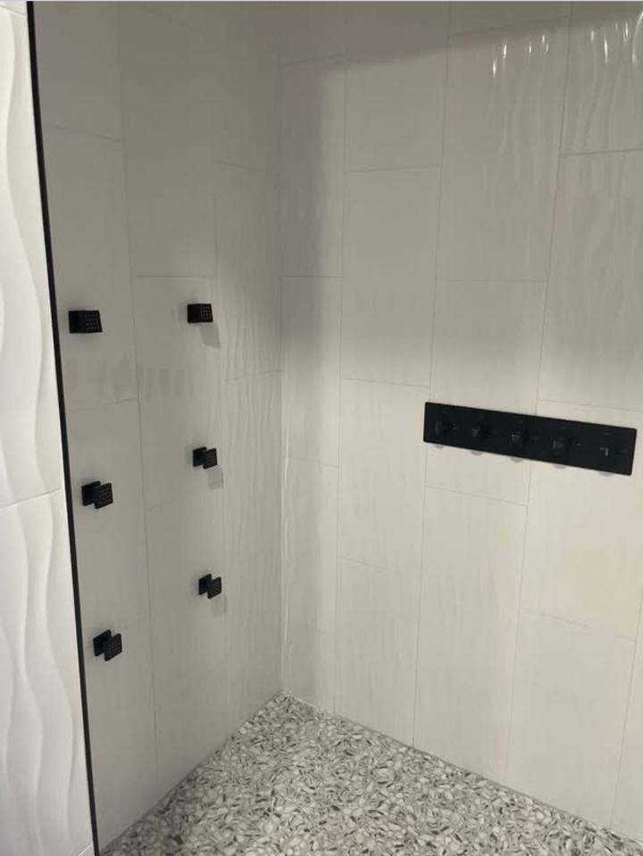 Wave-pattern tile shower with black body sprays and pebble floor